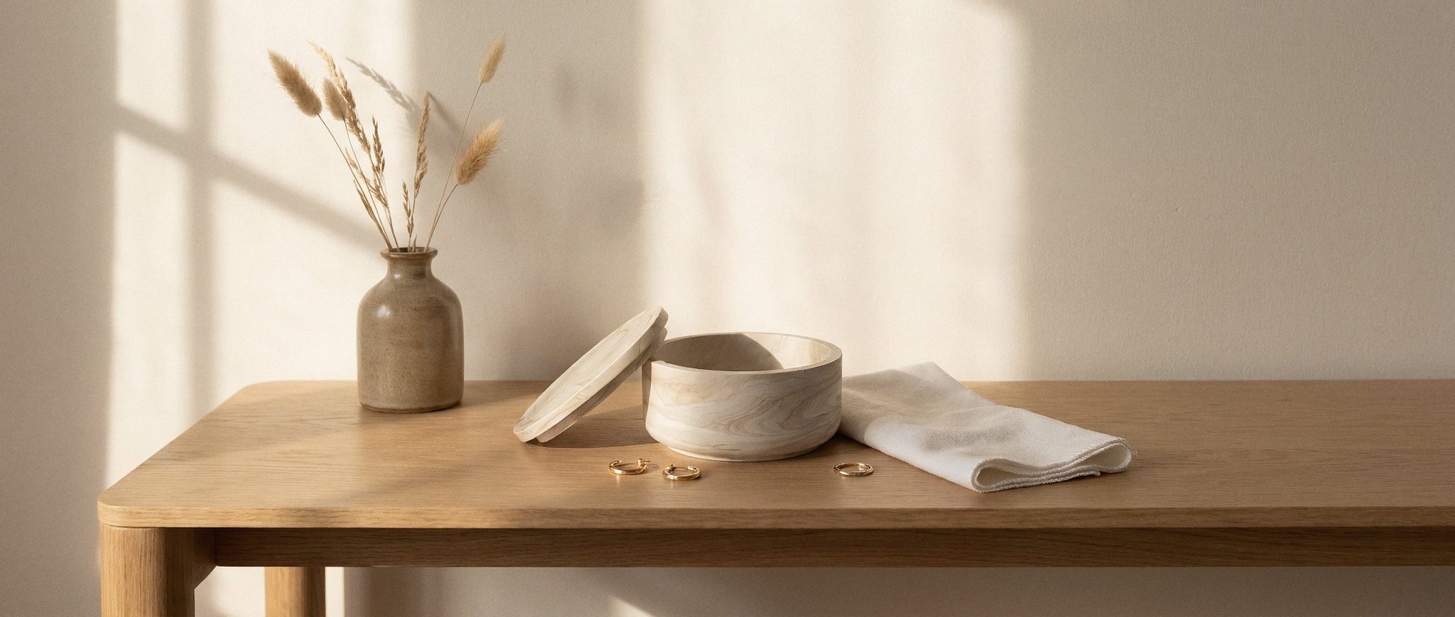 Cream marble Keepsake Bowl with its lid resting beside it, gold earrings and a folded cotton cloth on an oak console in afternoon sun